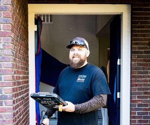 Experienced Grace Moving crew member providing moving packing services poses with tools at front door of brick California home
