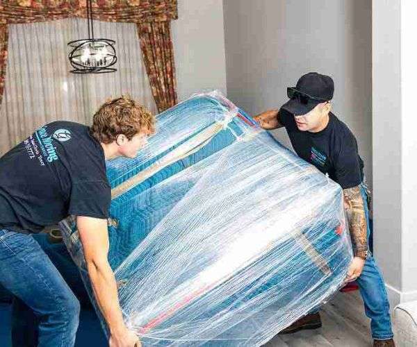 Two professional movers lifting furniture wrapped in a moving blanket.