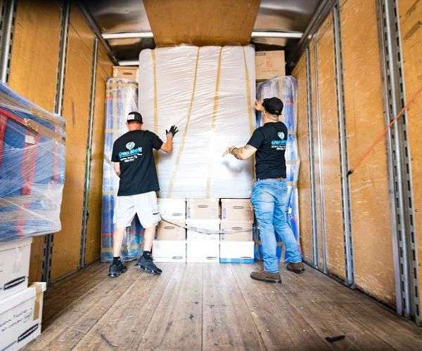 Professional packing services crew from Grace Moving securing shrink-wrapped mattress atop labeled moving boxes inside loaded truck
