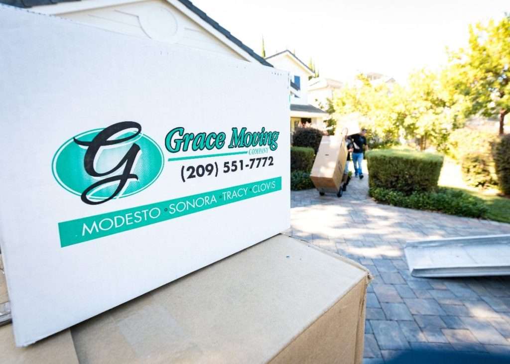 A stack of boxes with one on top and the Grace Moving logo with Biola movers carrying boxes in the background. 